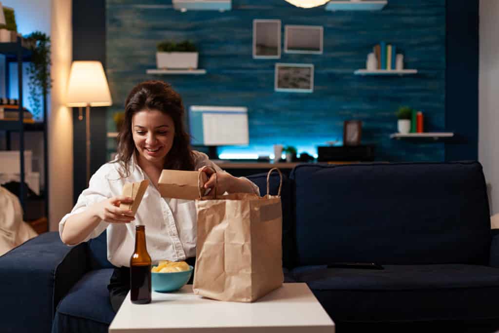 smiling cheerful woman unpacking tasting fast food home delivered sitting on couch